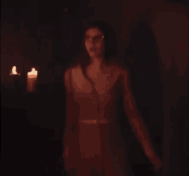 a woman is standing in a dark room with a candle in the background .