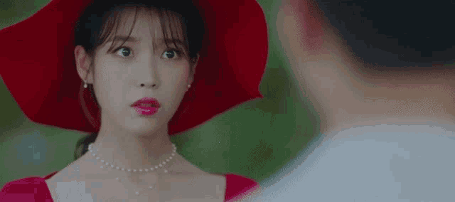 a woman wearing a red hat and a pearl necklace is standing next to a man .