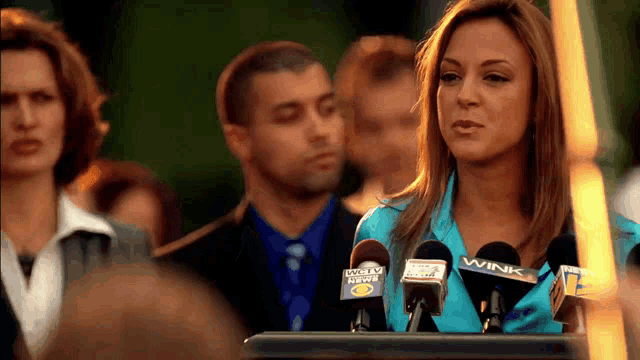 a woman stands behind a podium with microphones that say wink