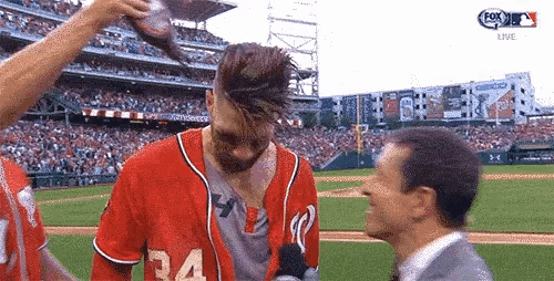 a baseball player wearing a red jersey with the number 34 on it is being interviewed by a man in a suit .