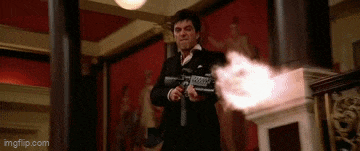 a man in a suit is holding a gun in a room with a red wall .