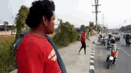 a man wearing a red shirt that says ' easy rider ' on it stands on a sidewalk