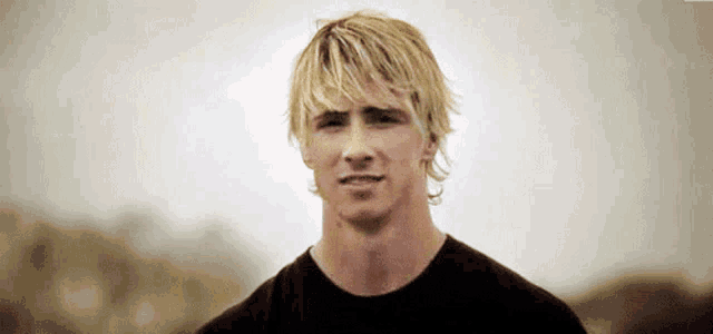 a man with blonde hair is wearing a black shirt and looking at the camera