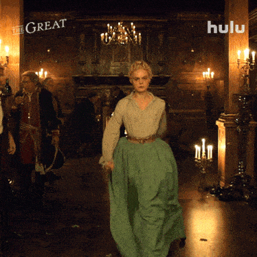 a woman in a green dress is walking in a hallway with candles and a sign that says hulu