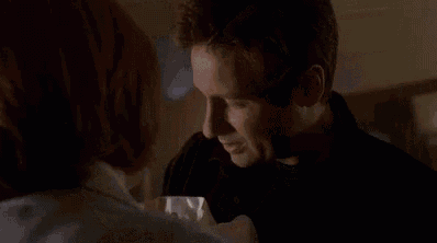 a man and a woman are looking at each other . the woman is wearing a blue sweater and a white shirt .