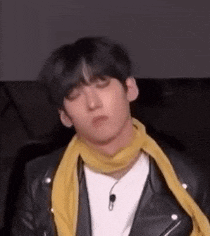 a young man wearing a yellow scarf and a leather jacket is making a funny face .