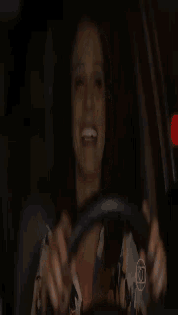 a woman is smiling while holding a steering wheel in a car