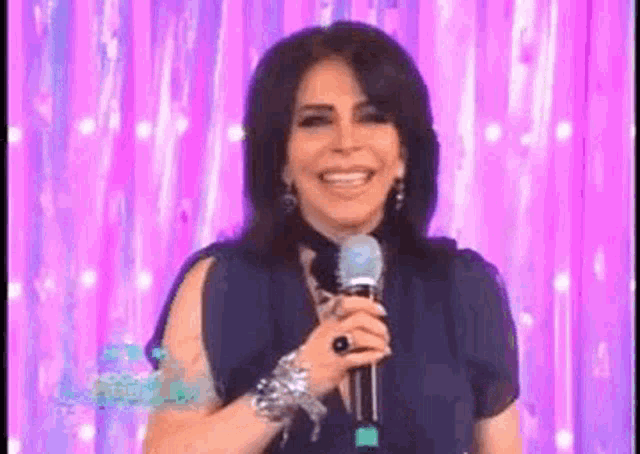 a woman is holding a microphone and smiling in front of a purple curtain