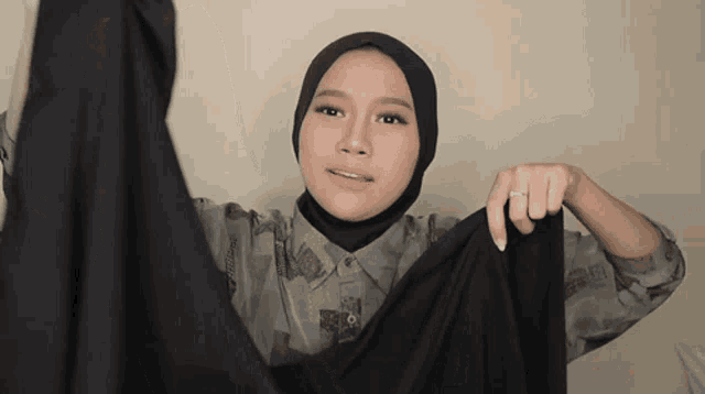 a woman wearing a hijab and a ring is holding a black cloth