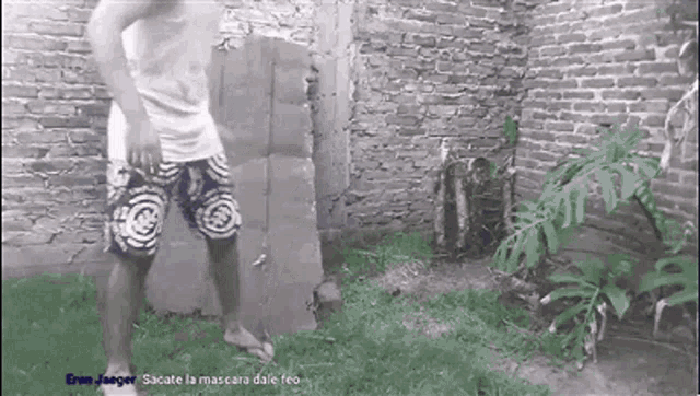 a man in shorts is standing in front of a brick wall in a yard .