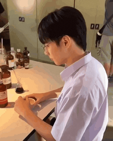 a young man is sitting at a table in a lab with bottles of chemicals .