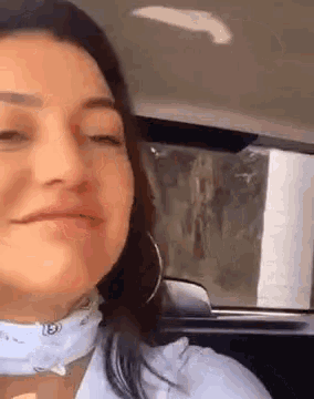 a woman is sitting in a car wearing a bandana around her neck and earrings .