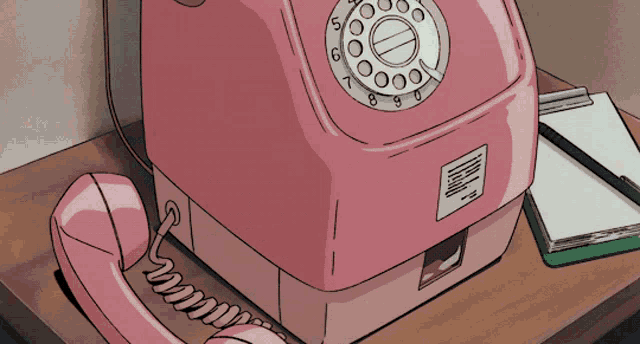 a pink telephone is on a table next to a notebook