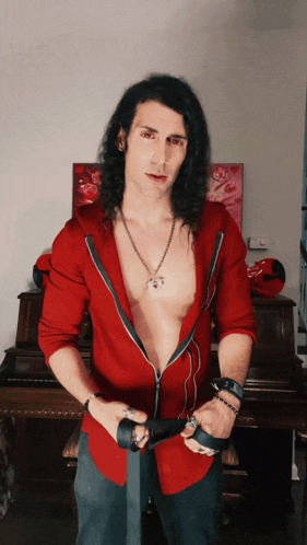 a man with long black hair is wearing a red shirt and a black belt