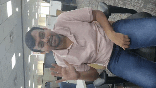 a man wearing glasses and a pink shirt is sitting on a chair in an office .