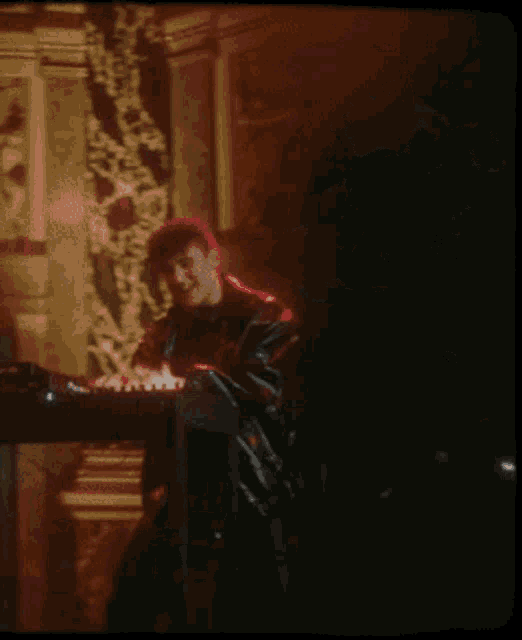 a man in a black jacket is playing a keyboard in a dark room