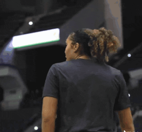 a woman in a black shirt stands in front of a basketball net