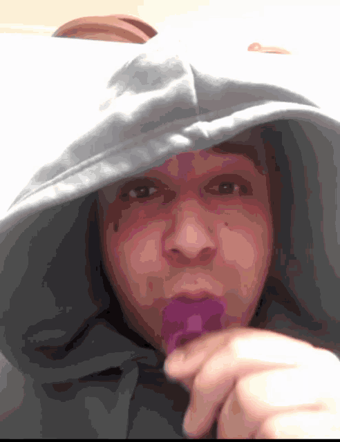a man wearing a hoodie is eating a purple candy .
