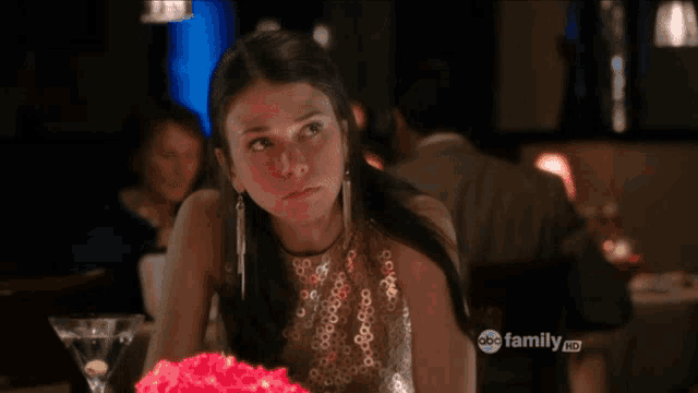 a woman sits at a table with a martini in front of her and a sign that says abc family