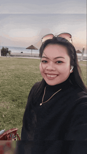 a woman wearing sunglasses and a necklace smiles for a picture