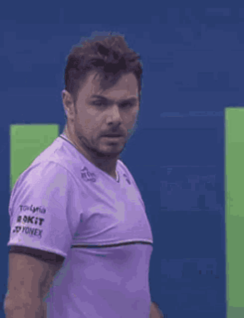 a man in a purple shirt is standing on a tennis court and looking at the camera .