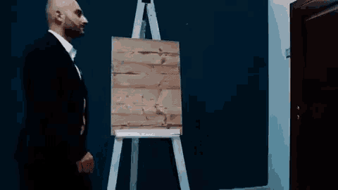 a man in a suit is standing in front of an easel with a wooden painting on it .