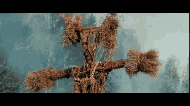 a scarecrow made out of branches and rope is in the middle of a forest