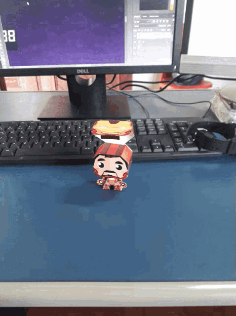 a dell computer monitor sits on a desk next to a paper toy of iron man