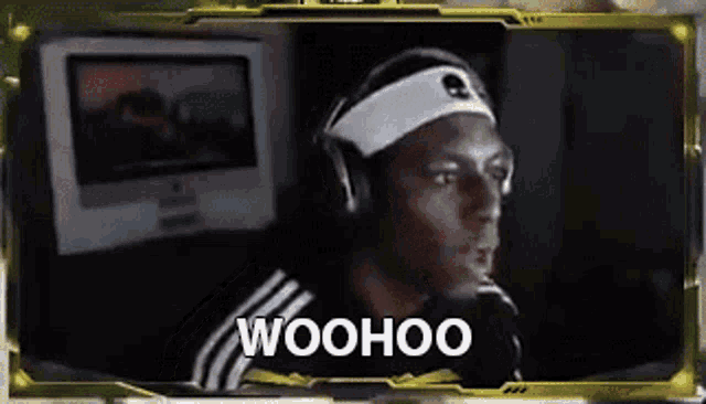 a man wearing headphones and a headband is sitting in front of a computer and says woohoo .