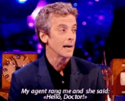 a man in a suit says " my agent rang me and she said hello doctor " in front of a clock