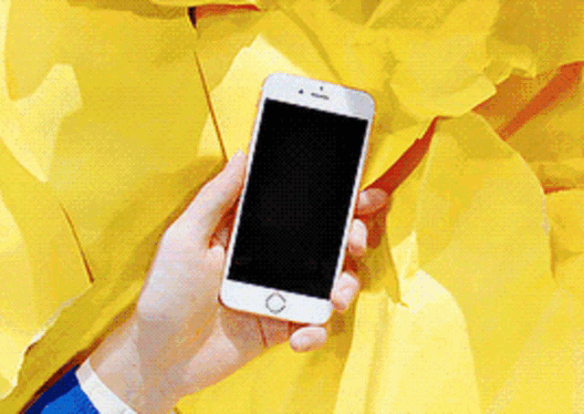 a person is holding a cell phone in front of a yellow wall