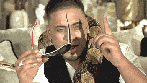 a man with a snake around his neck holds a pair of sunglasses in his mouth