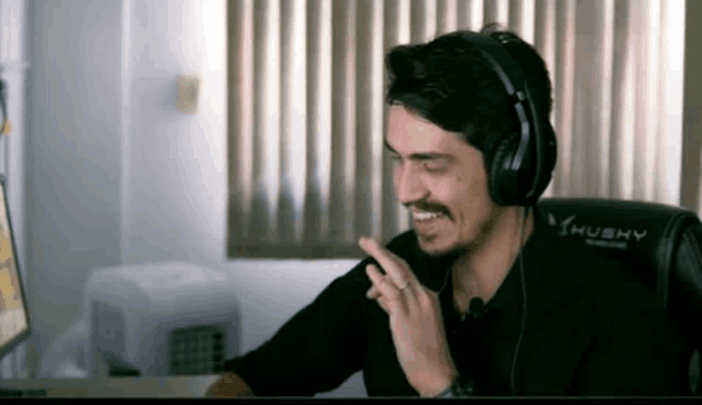 a man wearing headphones and a husky chair is smiling and pointing .