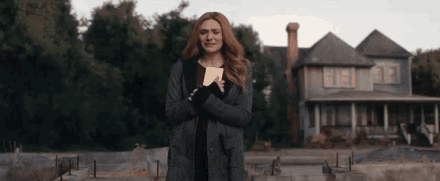a woman is standing in front of a house holding a piece of paper in her hands .