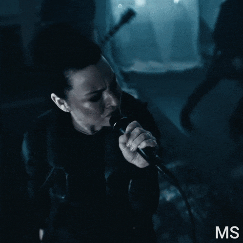 a woman singing into a microphone with the letters ms on the bottom right