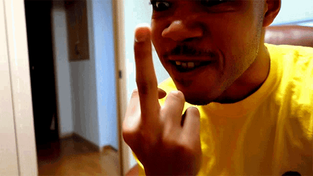 a man in a yellow shirt is making a middle finger gesture