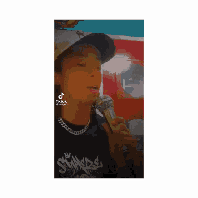 a young man singing into a microphone with tik tok written on the bottom right