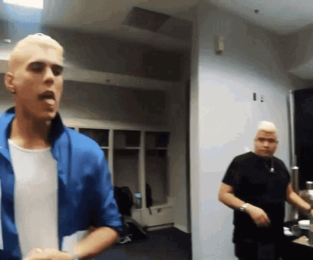 a man with blonde hair is sticking his tongue out while another man looks on