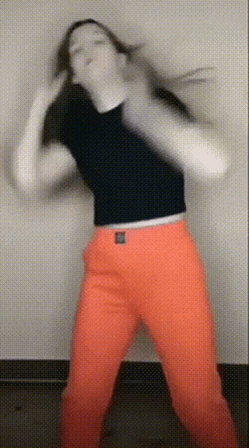 a woman wearing orange pants and a black top is dancing