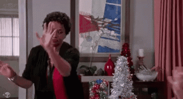 a woman is dancing in a living room in front of a christmas tree and a painting .