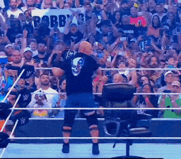 a wrestler with a skull on his back stands in front of a crowd with a sign that says " robby "
