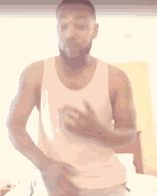 a man in a white tank top is standing on a bed