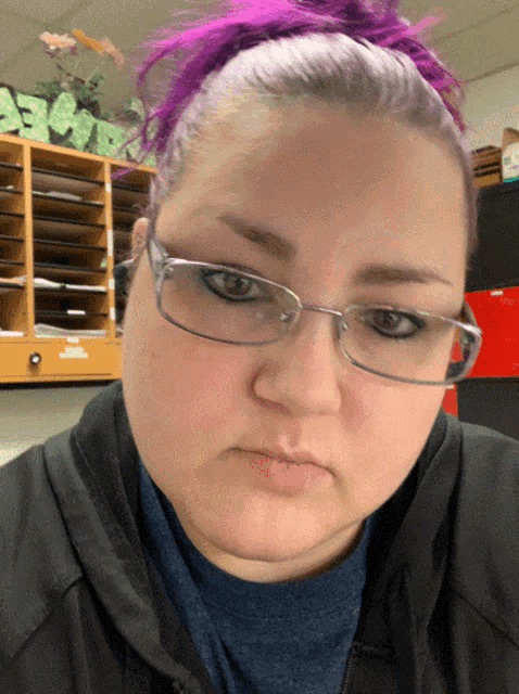 a woman with purple hair and glasses looks serious