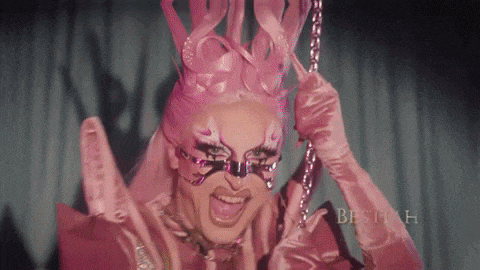 a drag queen is wearing a pink costume and holding a chain in her hand .