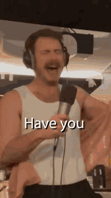 a man wearing headphones and a white tank top is singing into a microphone and laughing .