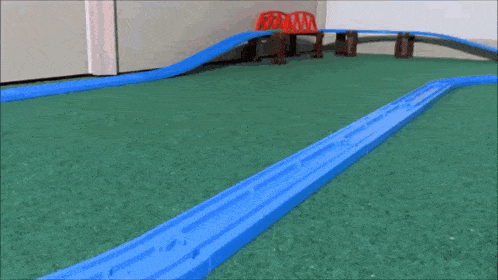 a toy fire truck is driving down a train track on a green carpet .