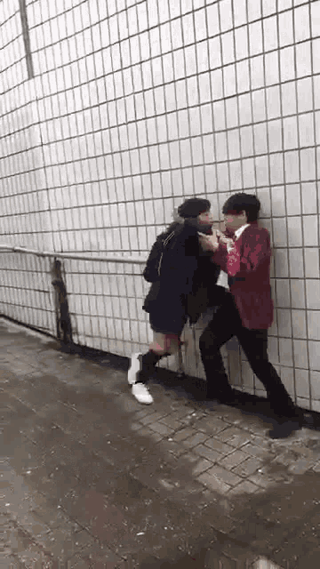 a man and a woman are fighting each other in front of a tiled wall .