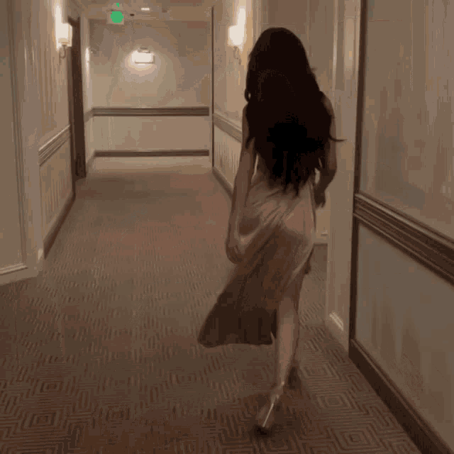 a woman in a white dress is walking down a hallway with an exit sign on the wall