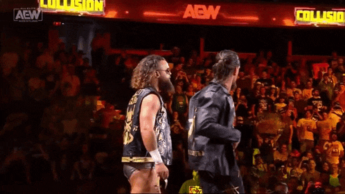 two wrestlers are walking in front of a crowd with a sign that says collision