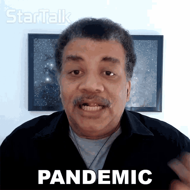 a man in a black shirt says pandemic in front of a picture